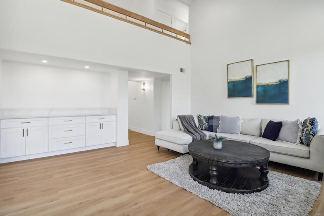 living area with light wood-type flooring, a towering ceiling, and visible vents