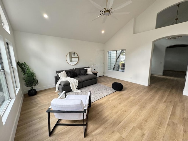 living area featuring arched walkways, high vaulted ceiling, baseboards, and light wood-style floors