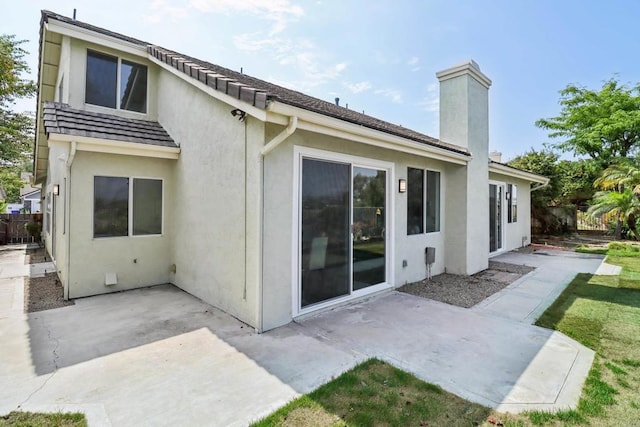 rear view of property featuring a patio, a chimney, fence, and stucco siding