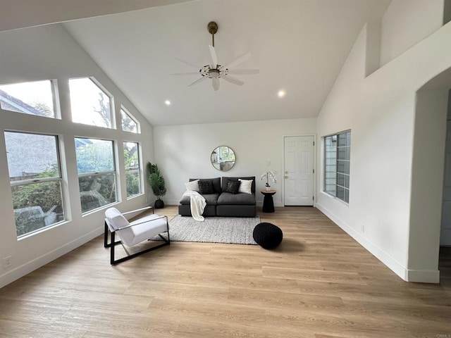 living room with light wood finished floors, baseboards, arched walkways, and high vaulted ceiling