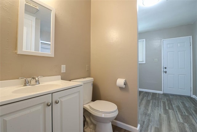 half bathroom with toilet, baseboards, wood finished floors, and vanity