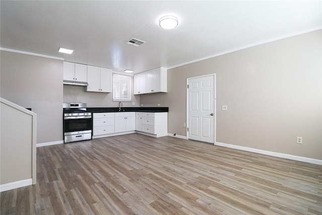 kitchen with dark countertops, light wood-style floors, gas stove, white cabinetry, and a sink