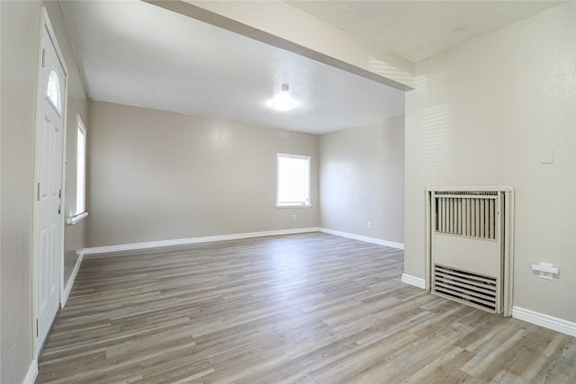 spare room featuring heating unit, light wood-style flooring, and baseboards