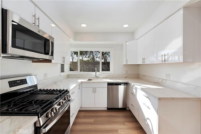 kitchen featuring light stone countertops, white cabinetry, appliances with stainless steel finishes, and light wood-style floors