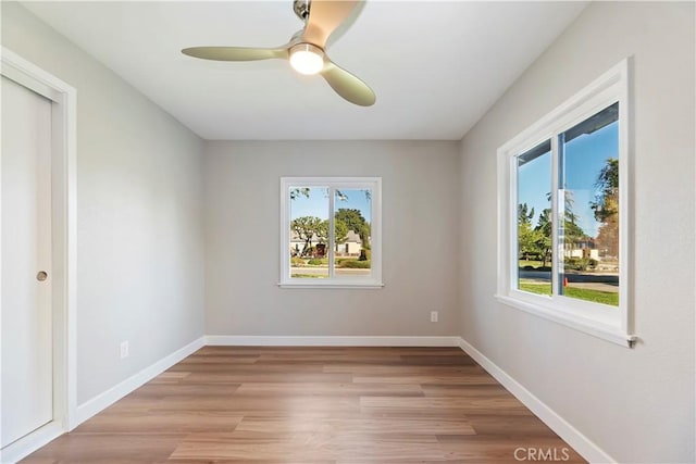 spare room with light wood-type flooring, a ceiling fan, and baseboards