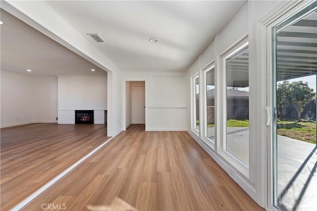 unfurnished living room with light wood-type flooring, visible vents, a wealth of natural light, and a glass covered fireplace