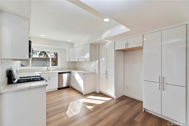 kitchen with dishwasher, gas range oven, a sink, and white cabinetry