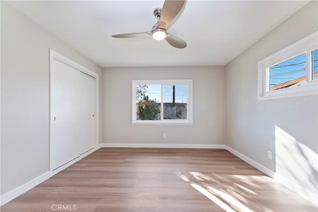 unfurnished bedroom featuring multiple windows, a closet, light wood-style flooring, and baseboards