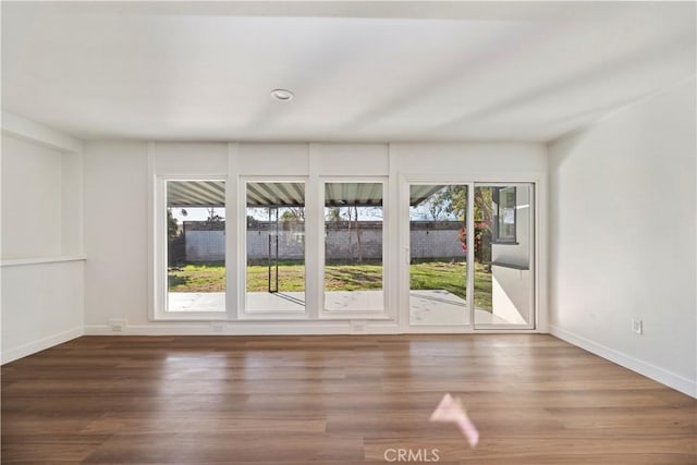 empty room featuring a healthy amount of sunlight, baseboards, and wood finished floors