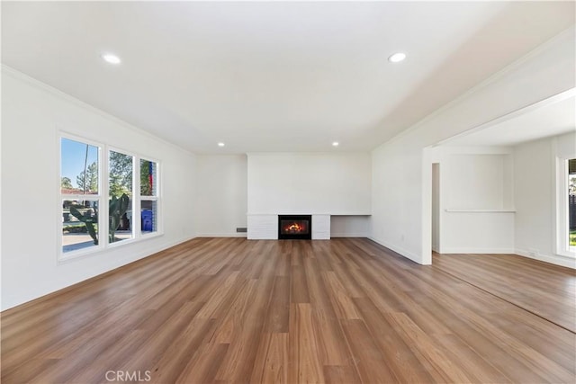 unfurnished living room with light wood-style floors, recessed lighting, crown molding, and a glass covered fireplace