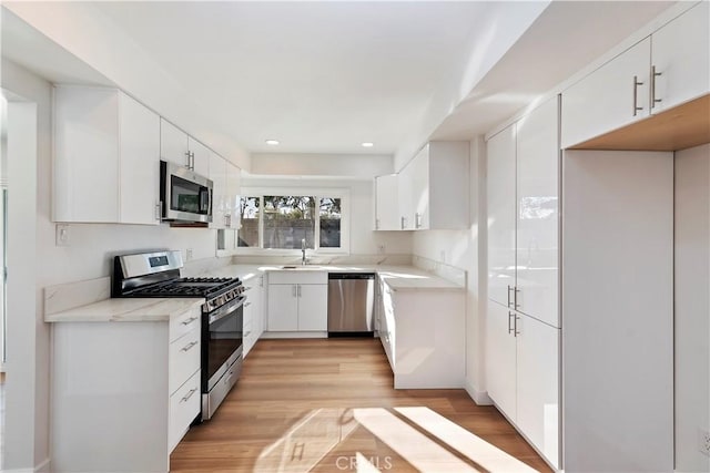 kitchen with appliances with stainless steel finishes, light countertops, white cabinets, and light wood-style floors