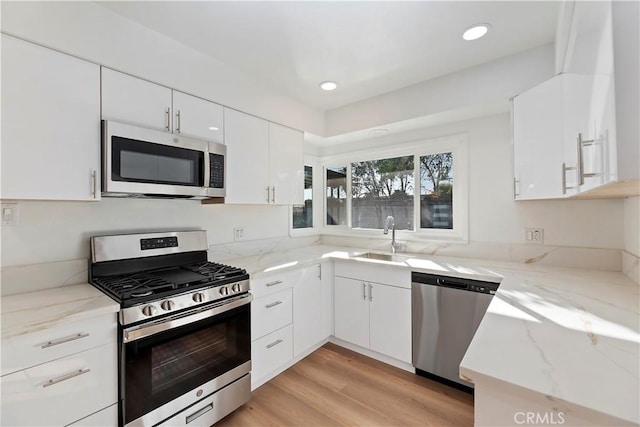 kitchen featuring appliances with stainless steel finishes, white cabinetry, a sink, and light stone countertops