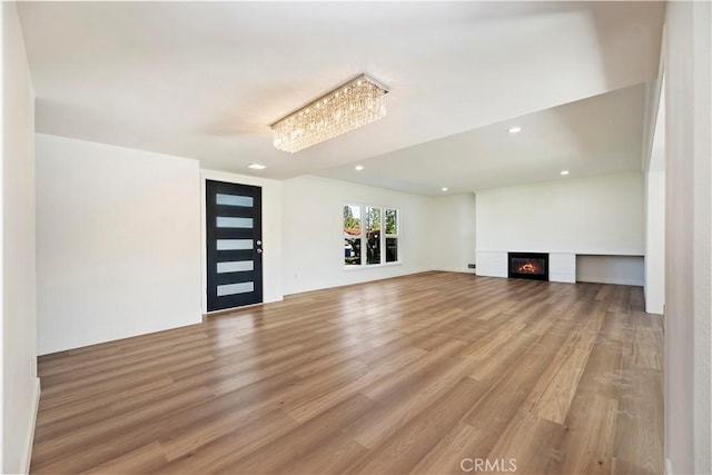 unfurnished living room featuring recessed lighting, a glass covered fireplace, and light wood-style floors