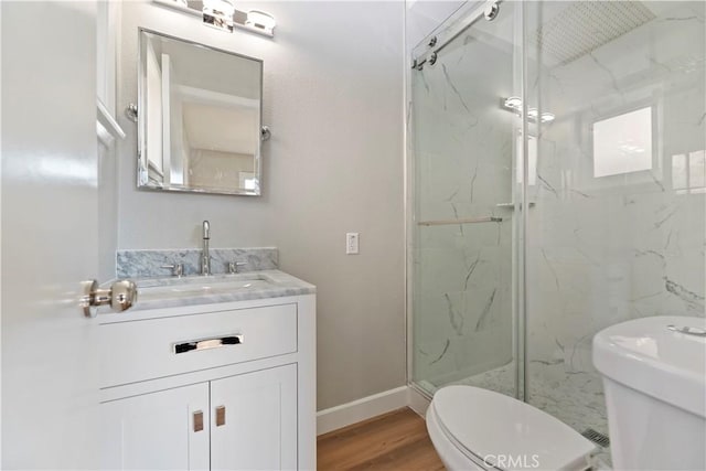 bathroom featuring toilet, wood finished floors, vanity, baseboards, and a marble finish shower