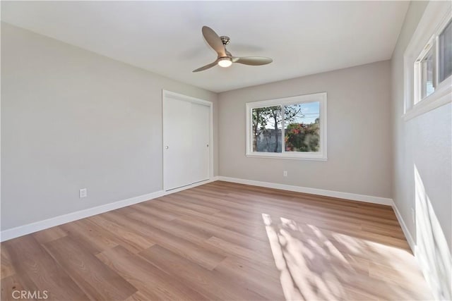 empty room featuring ceiling fan, light wood finished floors, and baseboards