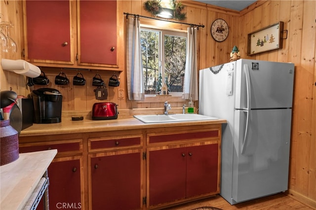 kitchen with light wood-style floors, freestanding refrigerator, light countertops, wood walls, and a sink