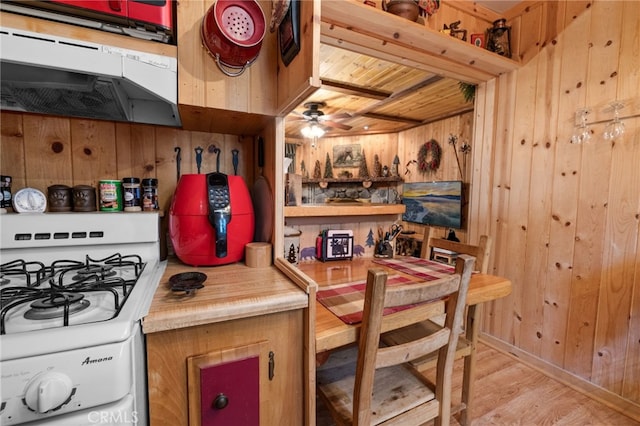 kitchen featuring ceiling fan, under cabinet range hood, wooden walls, white range with gas stovetop, and wood finished floors