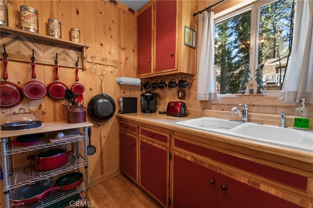 kitchen with light countertops, light wood finished floors, a sink, and wooden walls