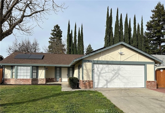 ranch-style home featuring brick siding, roof mounted solar panels, an attached garage, a front yard, and stucco siding