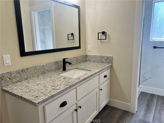 bathroom featuring a textured wall, baseboards, wood finished floors, and vanity