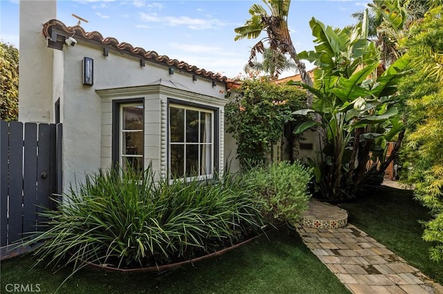 view of side of property with a tiled roof, fence, and stucco siding