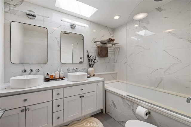 bathroom featuring a skylight, double vanity, a combined bath / shower with marble appearance, and a sink