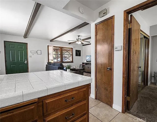 kitchen featuring tile countertops, beamed ceiling, light tile patterned flooring, and a ceiling fan