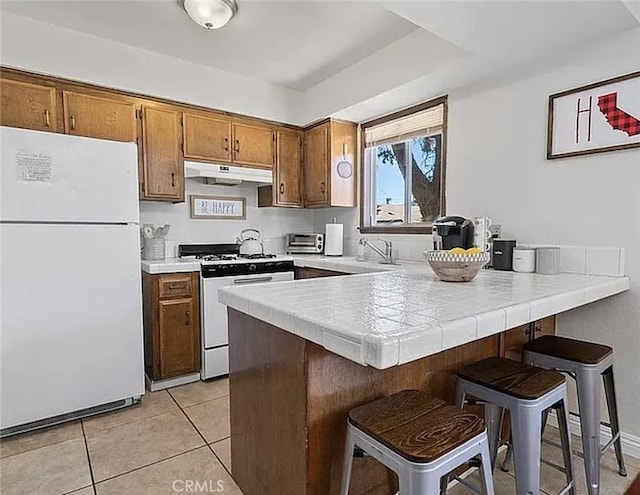 kitchen with a peninsula, white appliances, a kitchen bar, and under cabinet range hood