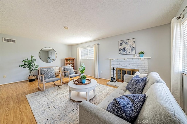 living room featuring a textured ceiling, a fireplace, visible vents, and light wood-style floors