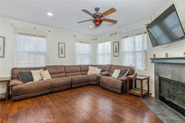 living room featuring a ceiling fan, a wealth of natural light, dark wood-style flooring, and a fireplace