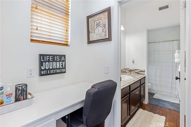 home office with dark wood-type flooring, built in desk, and visible vents