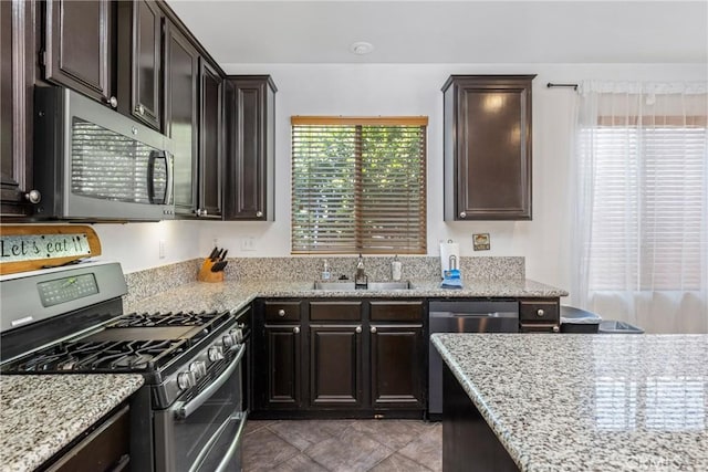 kitchen with appliances with stainless steel finishes, a sink, dark brown cabinetry, and light stone countertops