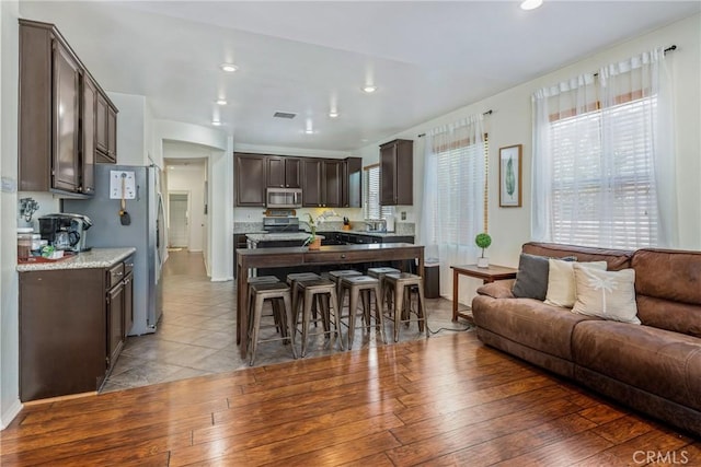 kitchen featuring a breakfast bar area, visible vents, open floor plan, dark brown cabinets, and appliances with stainless steel finishes