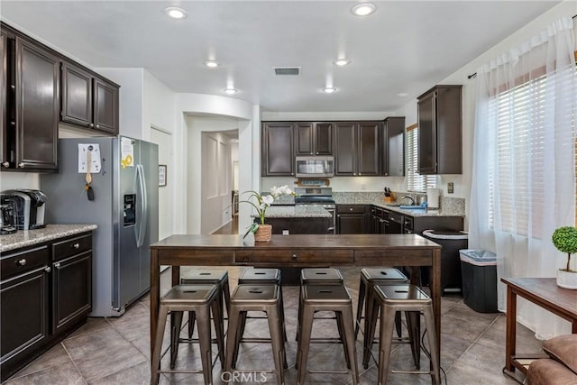 kitchen featuring dark brown cabinetry, appliances with stainless steel finishes, light stone countertops, a sink, and recessed lighting