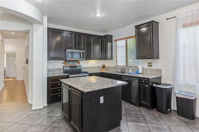 kitchen featuring arched walkways, light stone counters, recessed lighting, stainless steel appliances, and a kitchen island