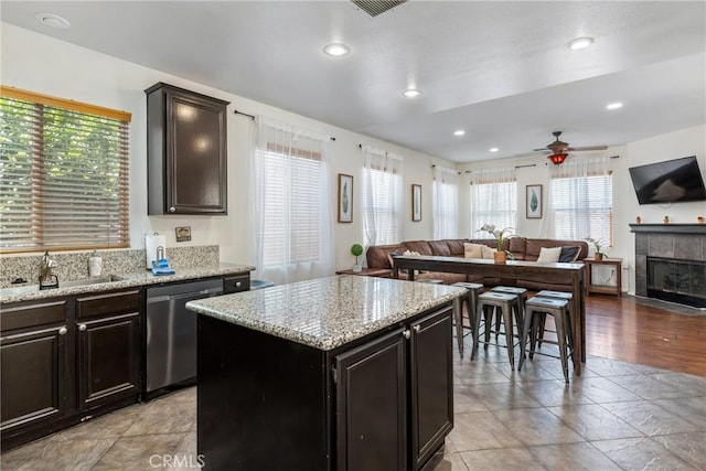 kitchen with a tiled fireplace, light stone counters, open floor plan, a center island, and stainless steel dishwasher