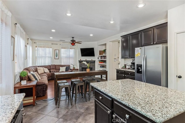 kitchen featuring stainless steel fridge, a kitchen island, open floor plan, a fireplace, and recessed lighting