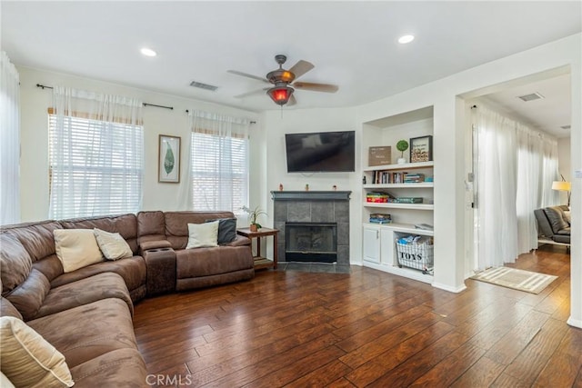 living room featuring built in shelves, a tile fireplace, recessed lighting, visible vents, and dark wood-style floors