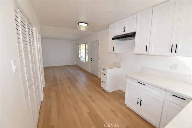 kitchen with light countertops, under cabinet range hood, light wood finished floors, and white cabinetry