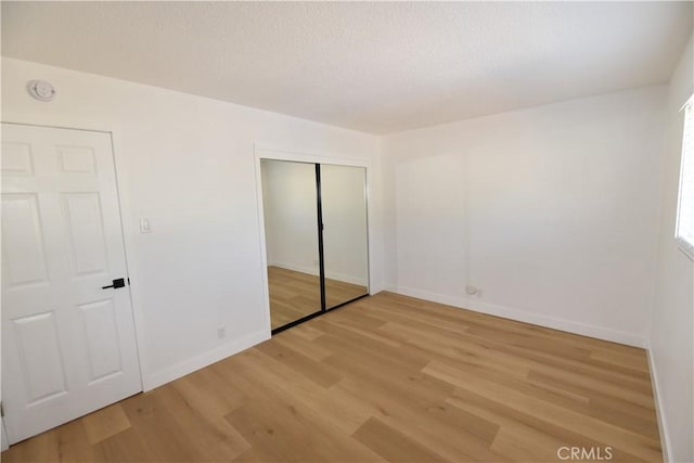 unfurnished bedroom with light wood-style floors, a closet, a textured ceiling, and baseboards