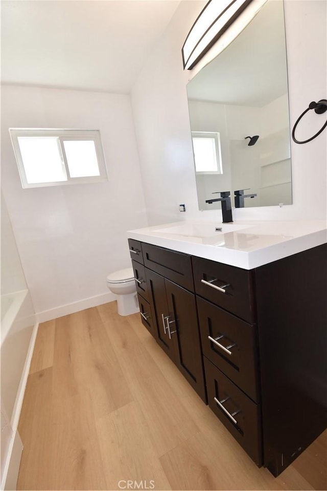 full bathroom with double vanity, toilet, a sink, wood finished floors, and baseboards