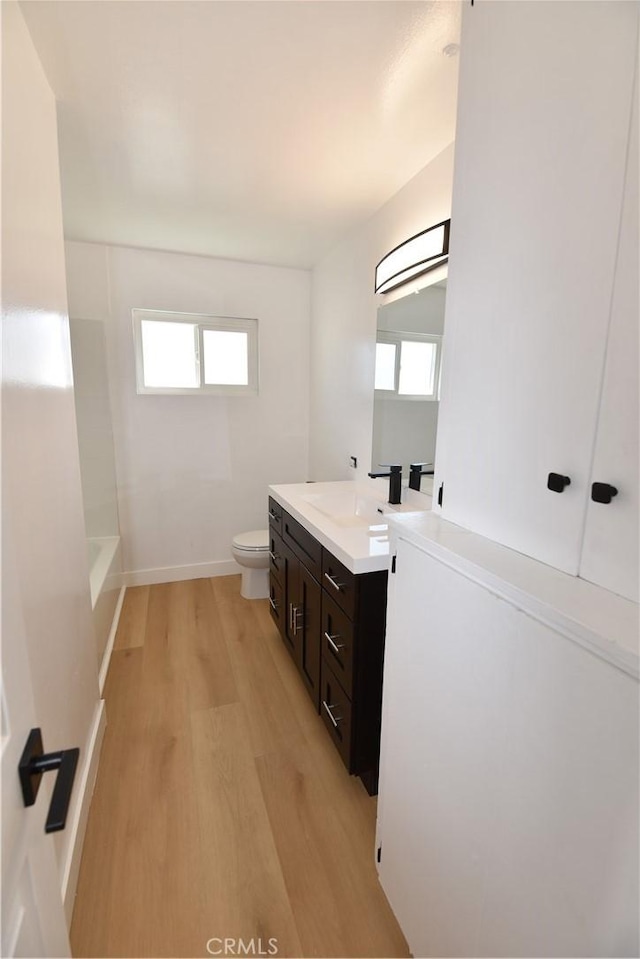 full bath with a wealth of natural light, vanity, toilet, and wood finished floors