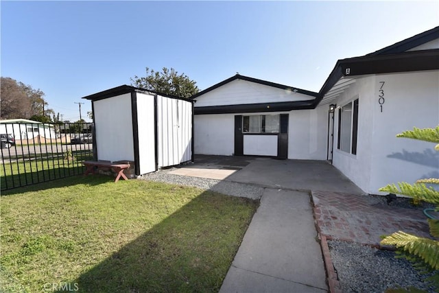 exterior space featuring an outbuilding, fence, a lawn, stucco siding, and a storage unit