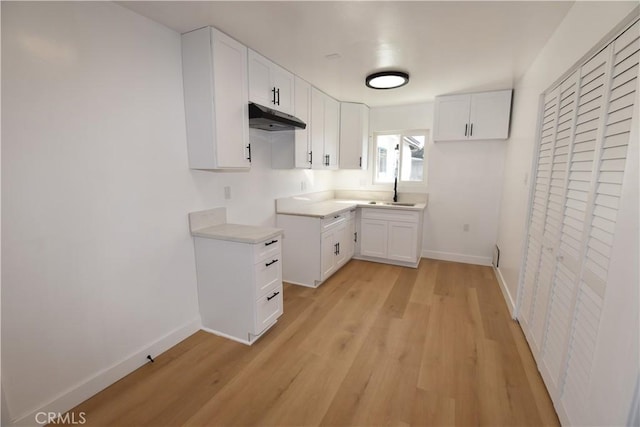 kitchen with baseboards, a sink, white cabinetry, and under cabinet range hood