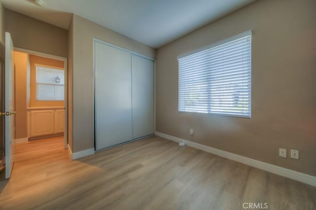 unfurnished bedroom featuring a closet, light wood-style flooring, and baseboards