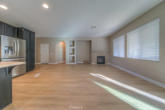 unfurnished living room featuring light wood-style floors, a fireplace, visible vents, and arched walkways