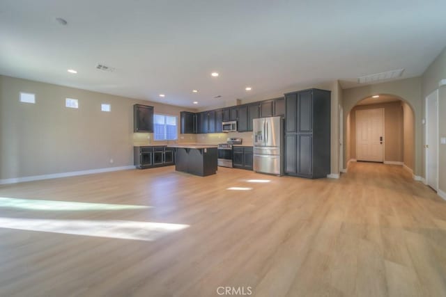 kitchen featuring visible vents, arched walkways, appliances with stainless steel finishes, open floor plan, and a center island