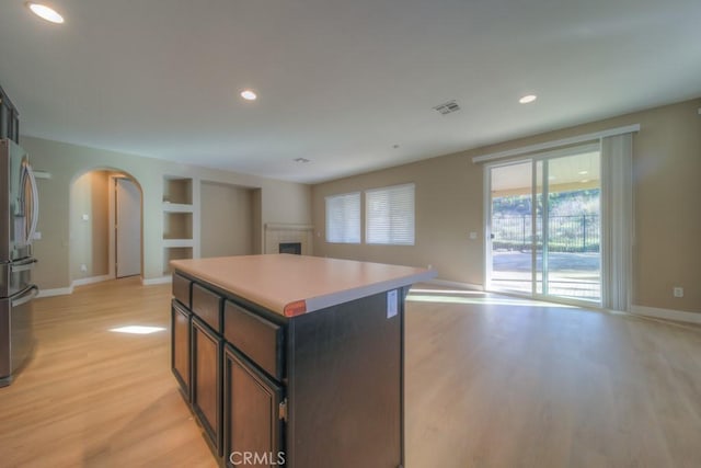 kitchen featuring arched walkways, a center island, stainless steel refrigerator with ice dispenser, visible vents, and open floor plan