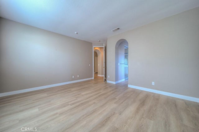 unfurnished room featuring light wood finished floors, visible vents, arched walkways, and baseboards