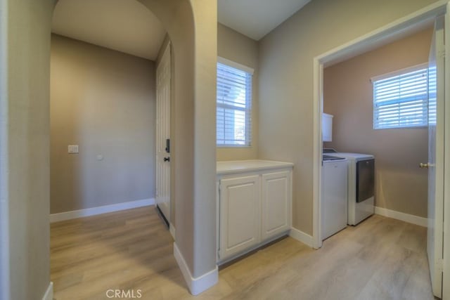 laundry room featuring baseboards, light wood finished floors, arched walkways, and washer and dryer